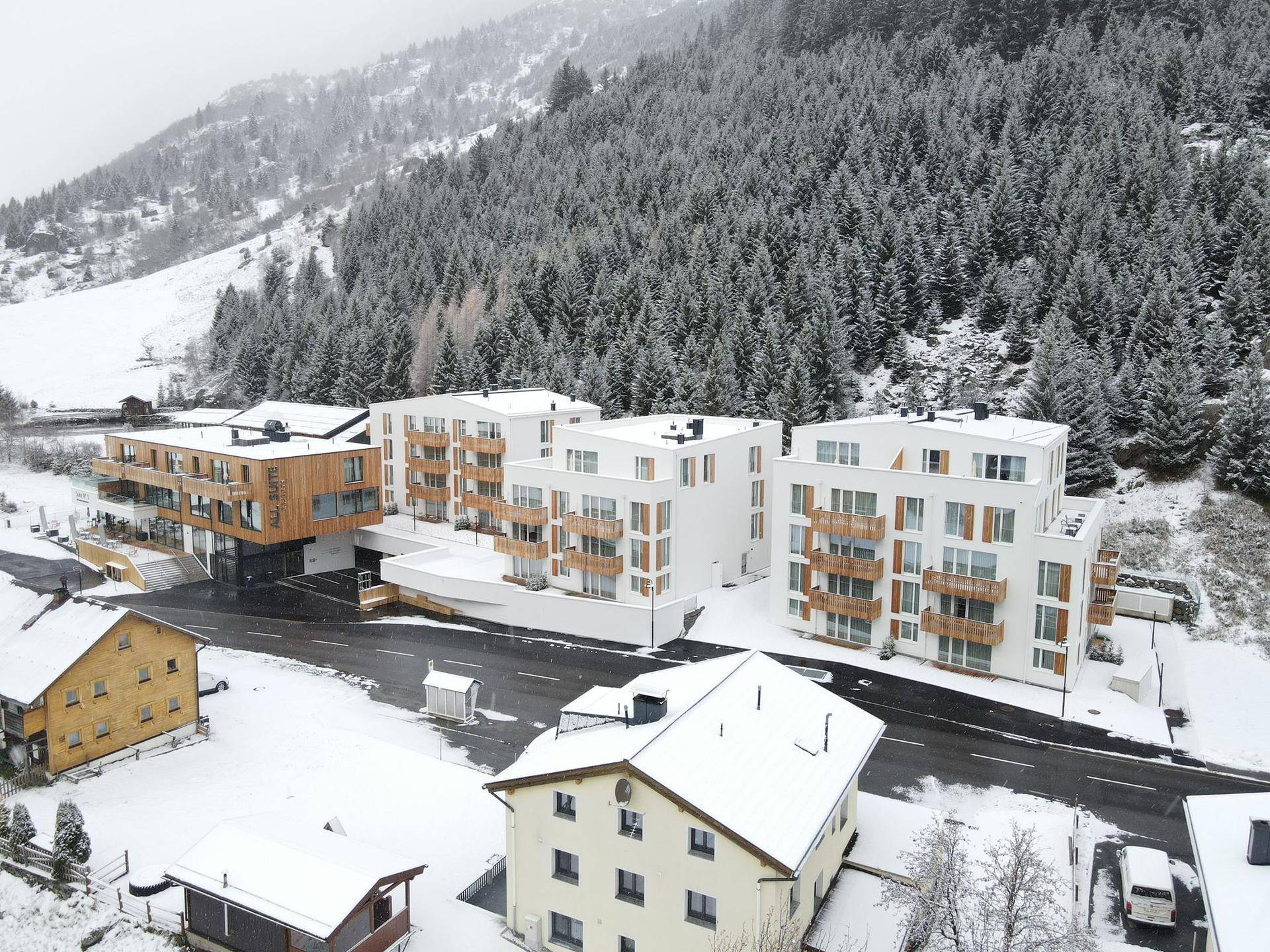 Moderne Apartmentgebäude mit Balkonen und Flachdächern, eingebettet in eine verschneite Berglandschaft.