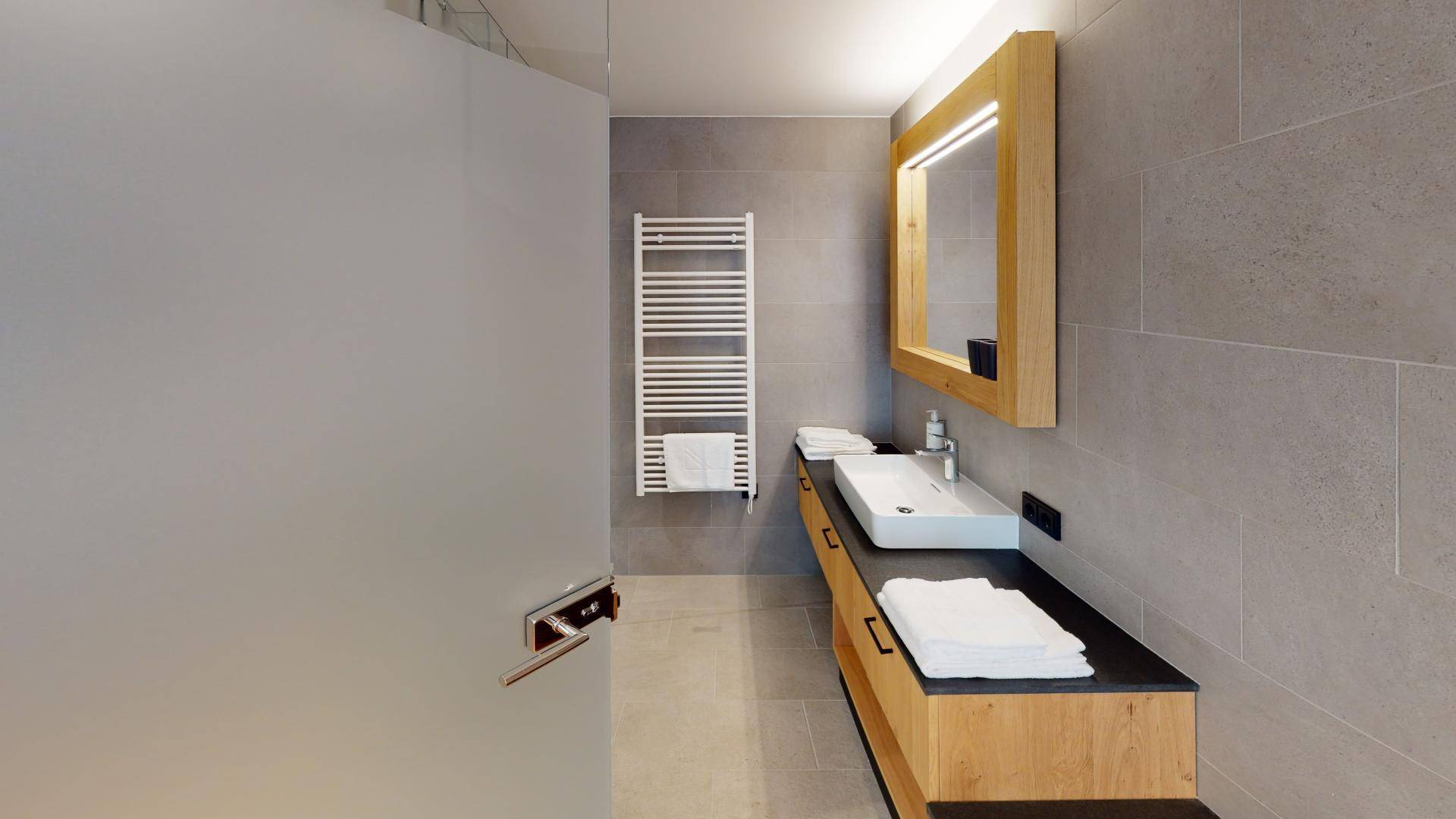 Elegantes Badezimmer mit modernem Waschtisch, großem Spiegel und beheiztem Handtuchhalter.