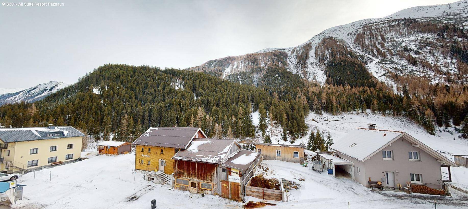 Verschneite Berglandschaft mit traditionellen Häusern und dichten Wäldern im Winter.