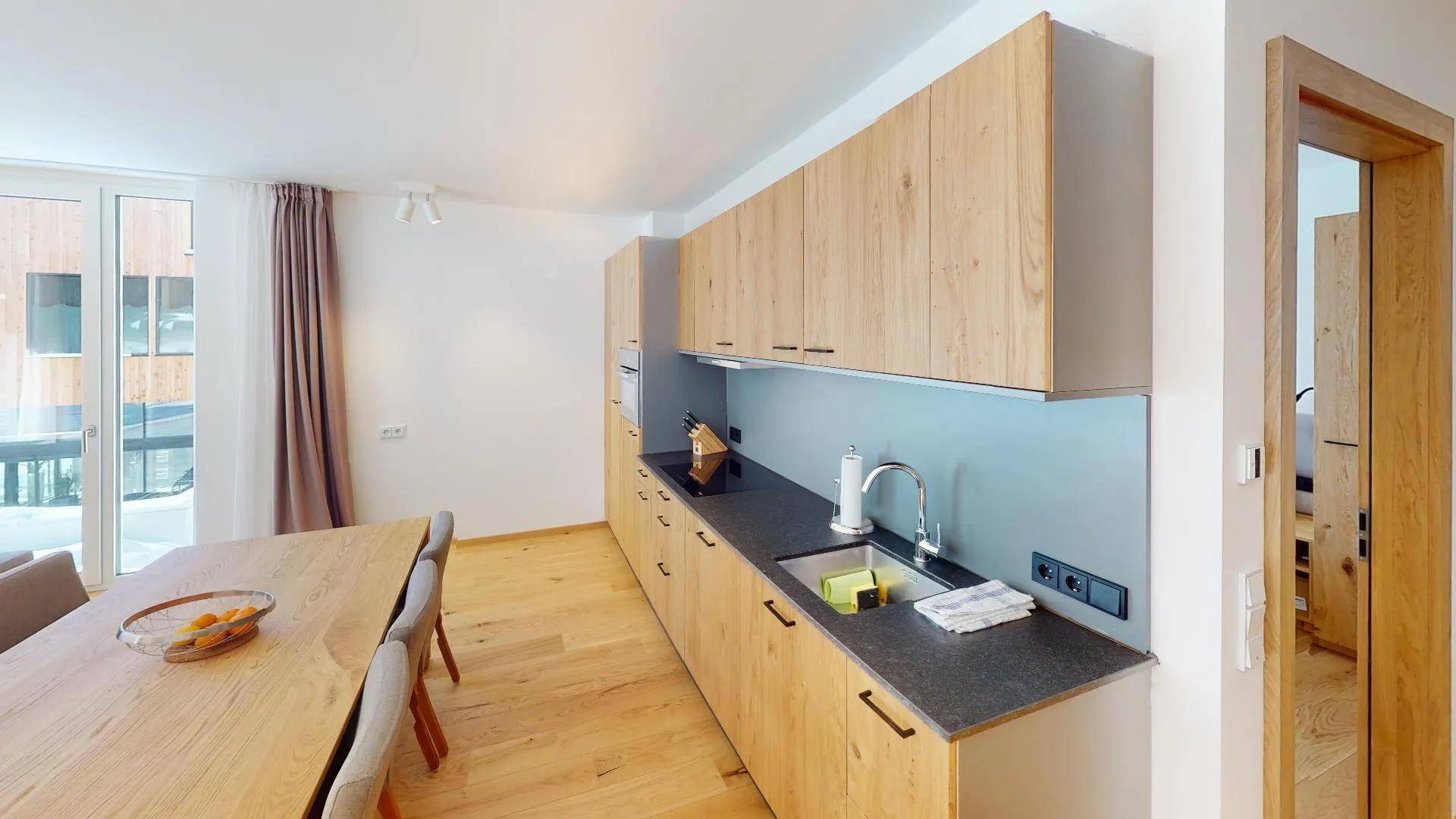 Moderne Holzküche mit dunkler Arbeitsplatte und Essbereich, offen zum Wohnbereich.