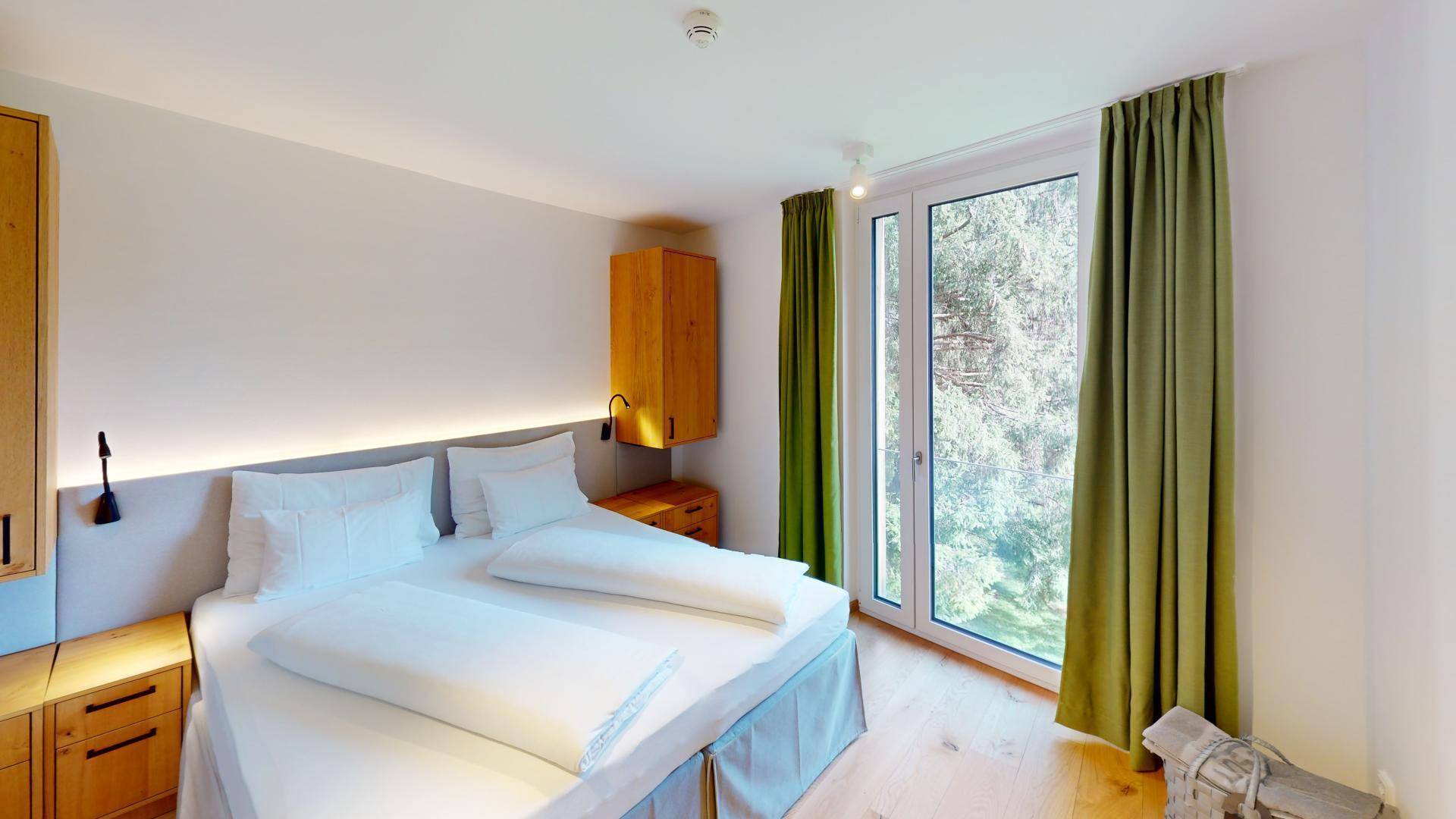Schlafzimmer mit Doppelbett, Holzboden und großen Fenstern mit Blick ins Grüne.
