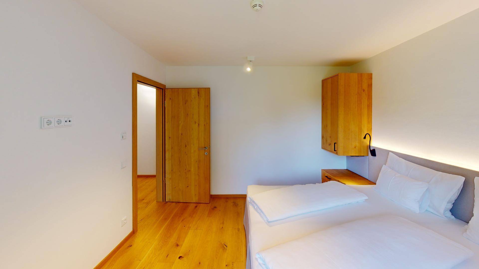 Helles Schlafzimmer mit Holzboden, Doppelbett und schlichten Holzmöbeln.