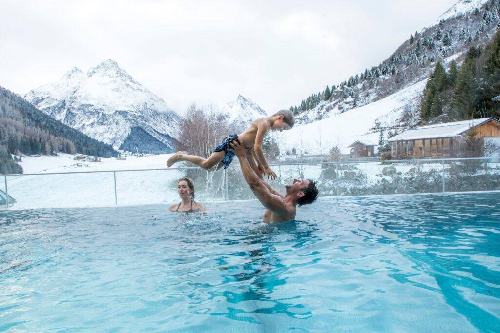 Familie genießt den beheizten Außenpool mit spektakulärem Blick auf die verschneiten Berge.