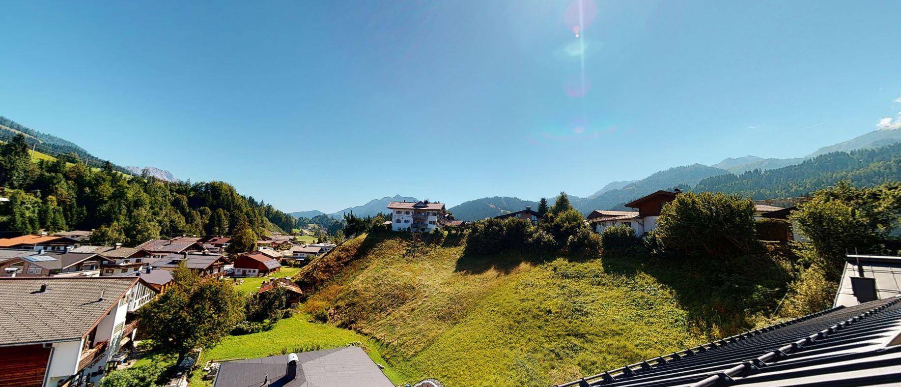 Weitläufige Aussicht auf sanfte grüne Hügel und ein Dorf, eingebettet in die Berglandschaft.