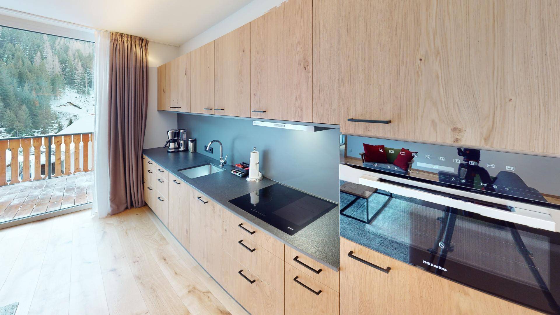 Moderne Holzküche mit Induktionskochfeld, Backofen und Zugang zu einem Balkon mit Bergblick.