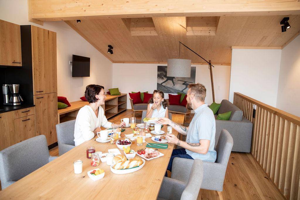 Familie genießt ein Frühstück in einem hellen, offenen Wohn-Essbereich mit Holzelementen und moderner Einrichtung.