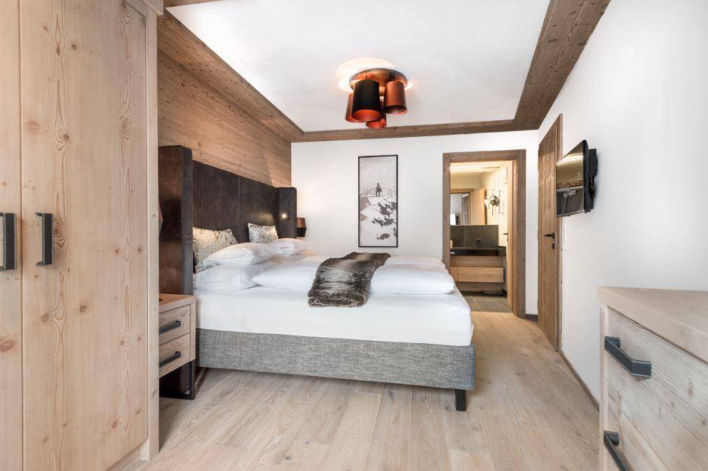 Gemütliches Schlafzimmer mit Holzwänden, großem Bett und Zugang zu einem modernen Bad en suite.