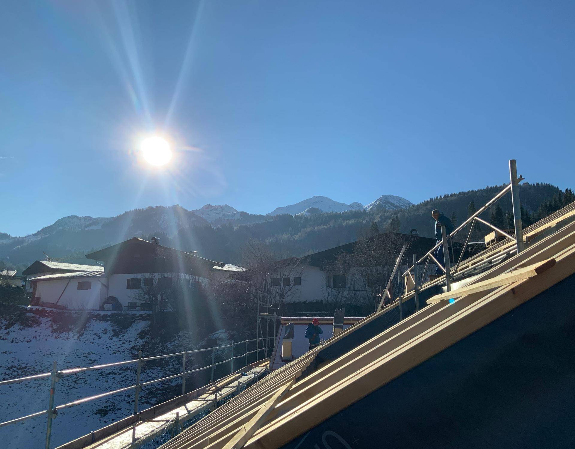Dachkonstruktion eines Neubaus mit Gerüst und sonnigem Bergblick im Winter.