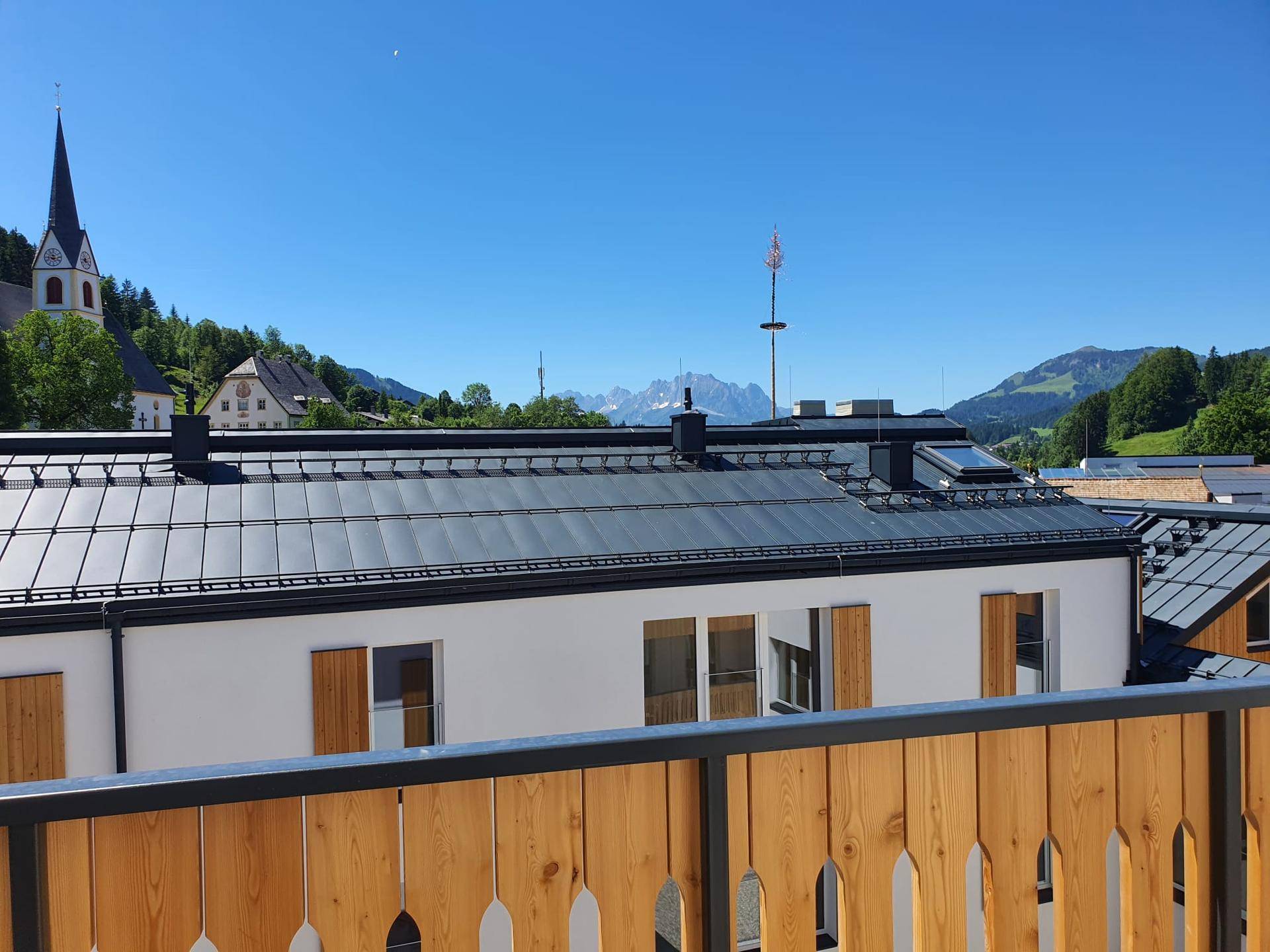 Blick von einem Balkon auf das Dach des Gebäudes, eine Kirche und die Berge.