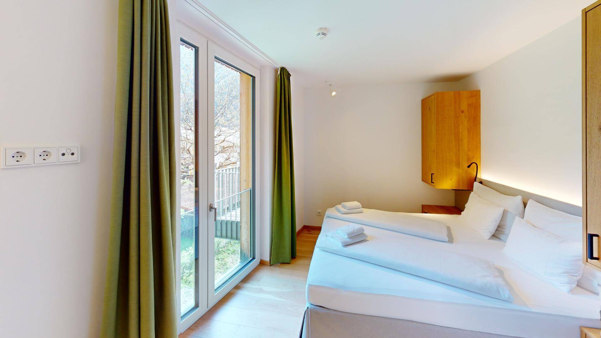 Schlafzimmer mit Doppelbett, Holzboden und Zugang zu einem französischen Balkon.