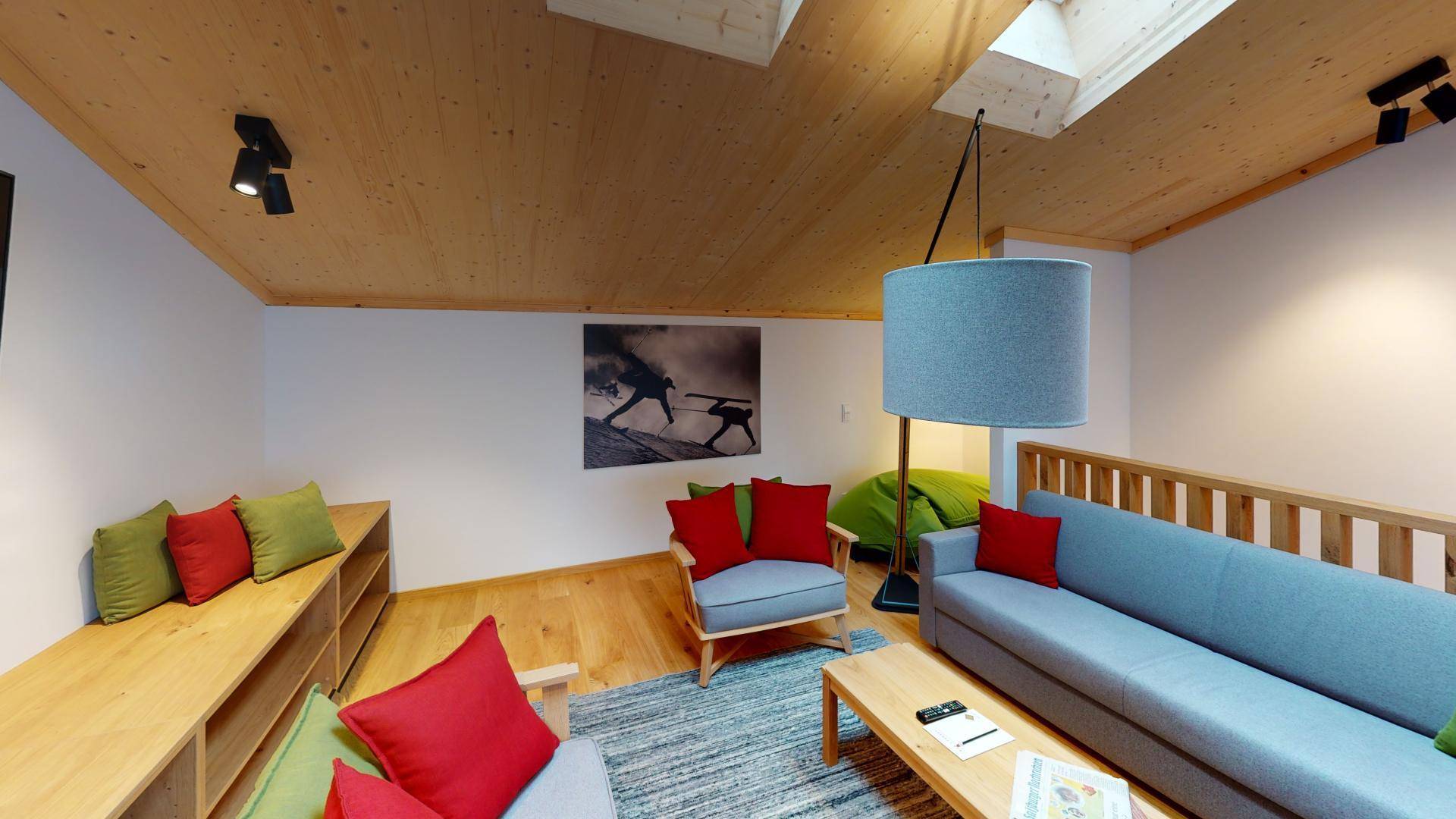 Gemütliches Wohnzimmer mit Holzbalkendecke, Dachfenstern und modernen Möbeln in warmen Farben.