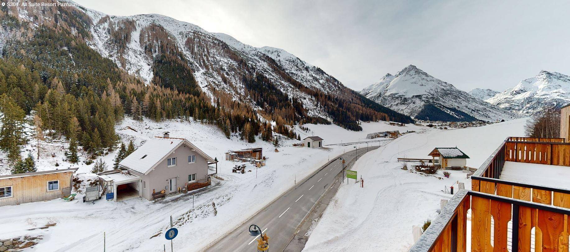 Panoramablick auf die verschneite Berglandschaft mit Häusern und einer Straße im Winter.