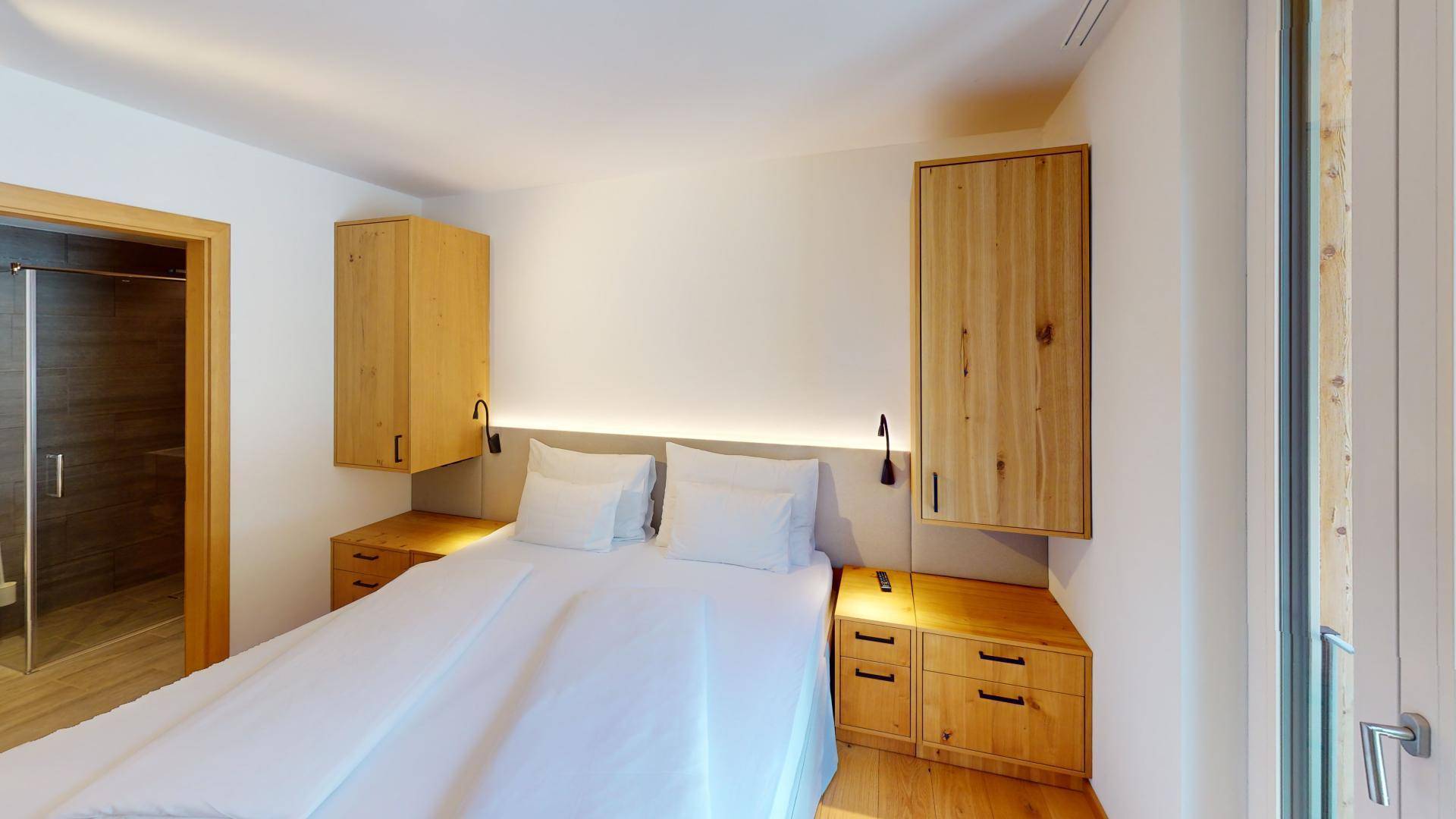 Schlafzimmer mit Doppelbett, Holzboden und Zugang zu einem angrenzenden Badezimmer.