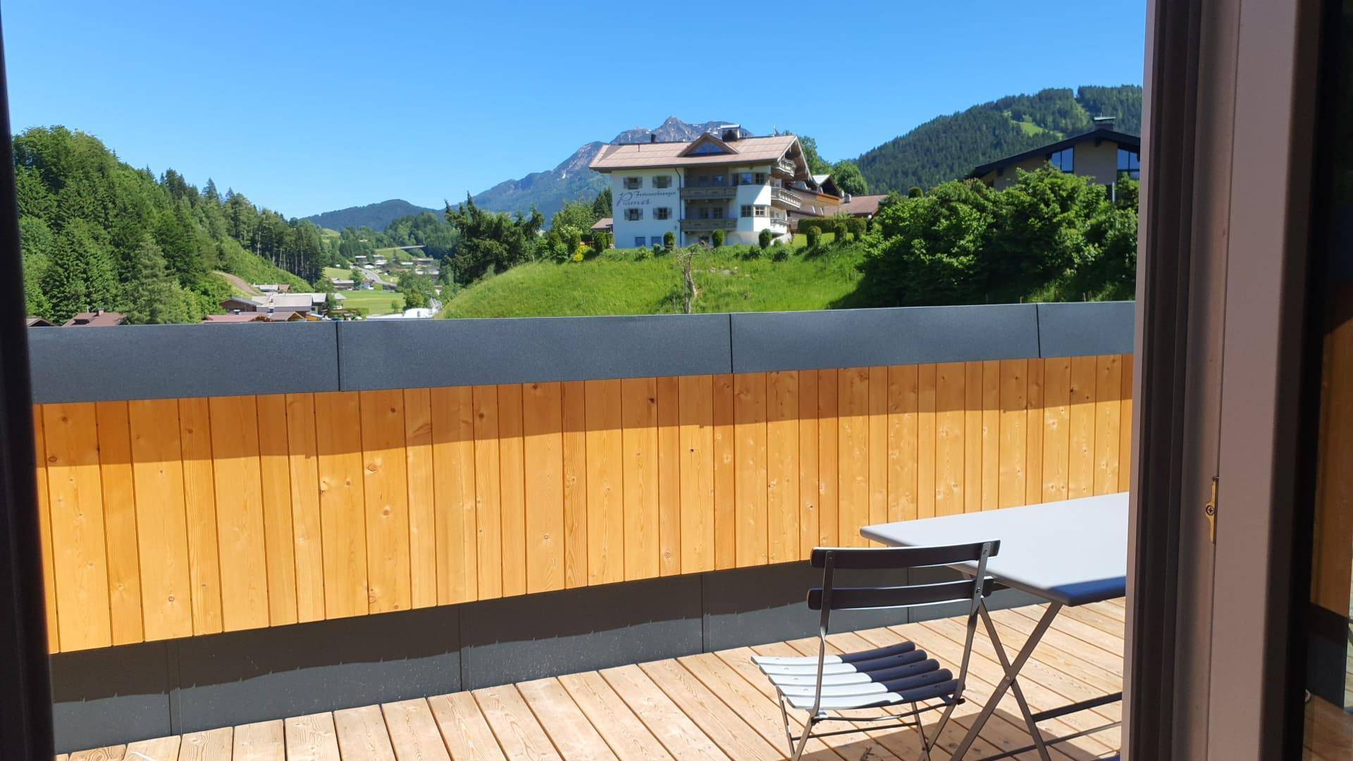 Sonnige Terrasse mit Holzboden, Sitzgelegenheiten und weitem Bergblick.