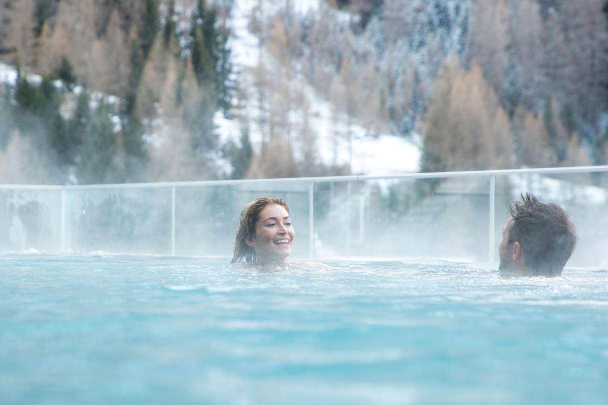 Zwei Personen genießen ein warmes Bad im dampfenden Außenpool mit Winterlandschaft.
