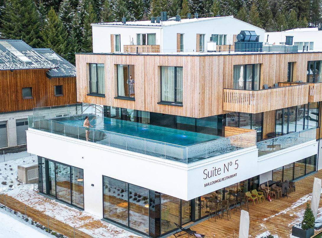 Moderne Architektur mit einem Infinity-Pool auf dem Dach und Holzfassade in verschneiter Umgebung.