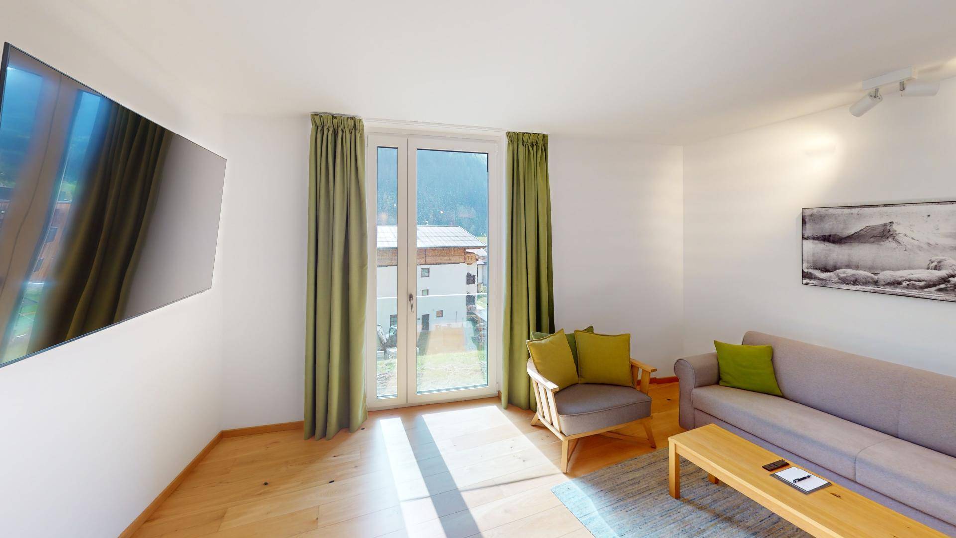 Gemütliches Wohnzimmer mit Sofa, Sessel und großen Fenstern, die viel Tageslicht hereinlassen.