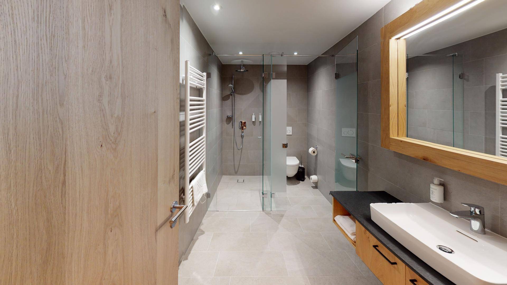 Modernes Badezimmer mit begehbarer Dusche, grauen Fliesen und einem beheizten Handtuchhalter.