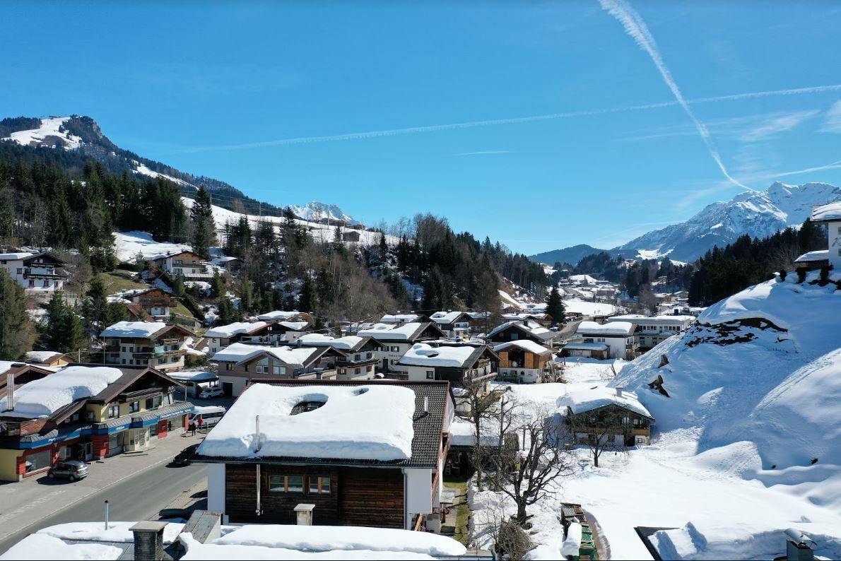 Panoramablick auf ein verschneites Bergdorf mit traditionellen Häusern und majestätischen Bergen im Hintergrund.