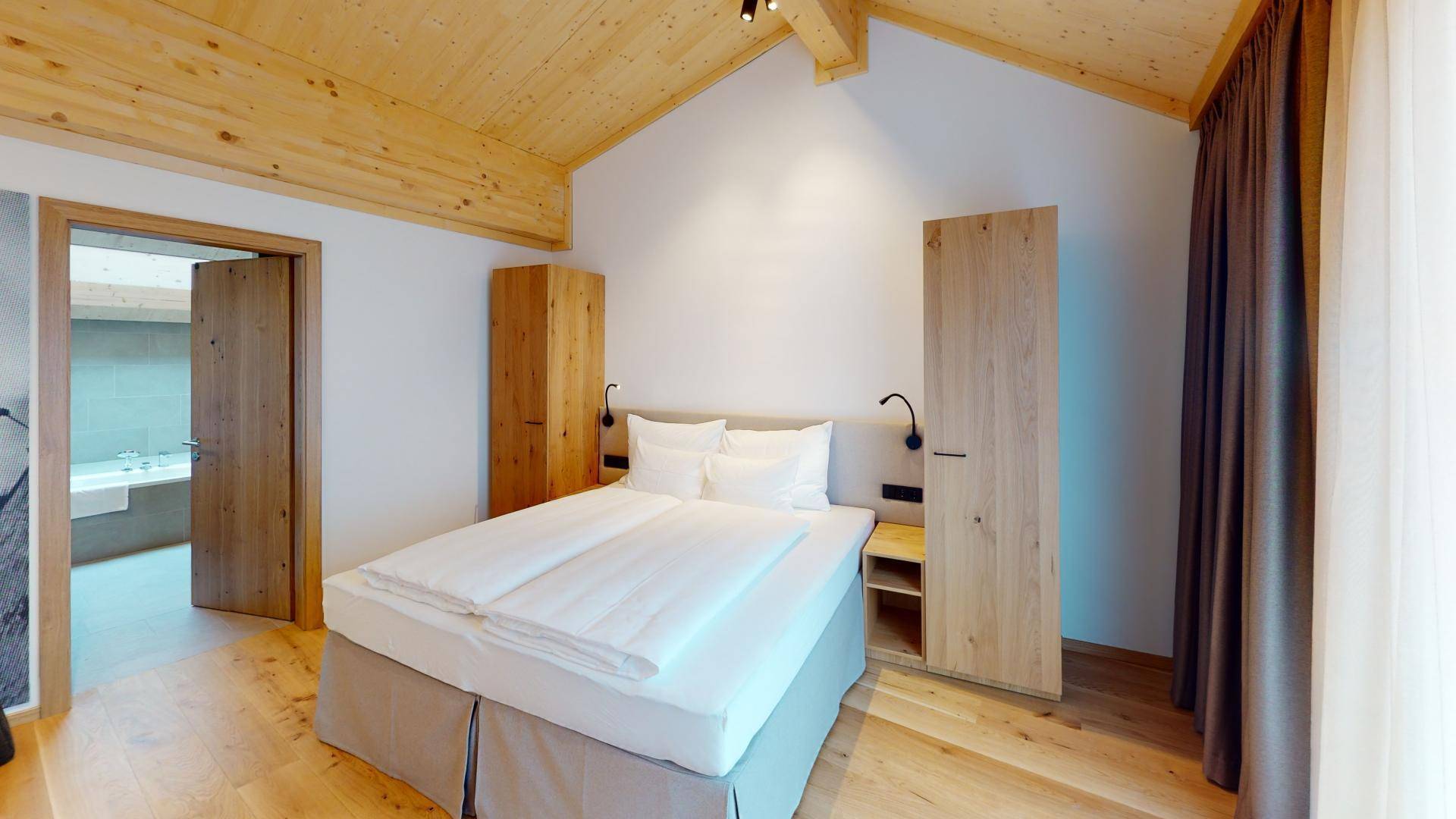 Geräumiges Schlafzimmer mit hoher, gewölbter Holzdecke, Holzboden und Zugang zum Badezimmer.