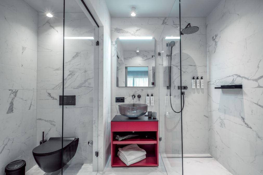 Modernes Badezimmer mit Marmorfliesen, begehbarer Dusche, wandhängendem WC und stilvollem roten Waschtisch.