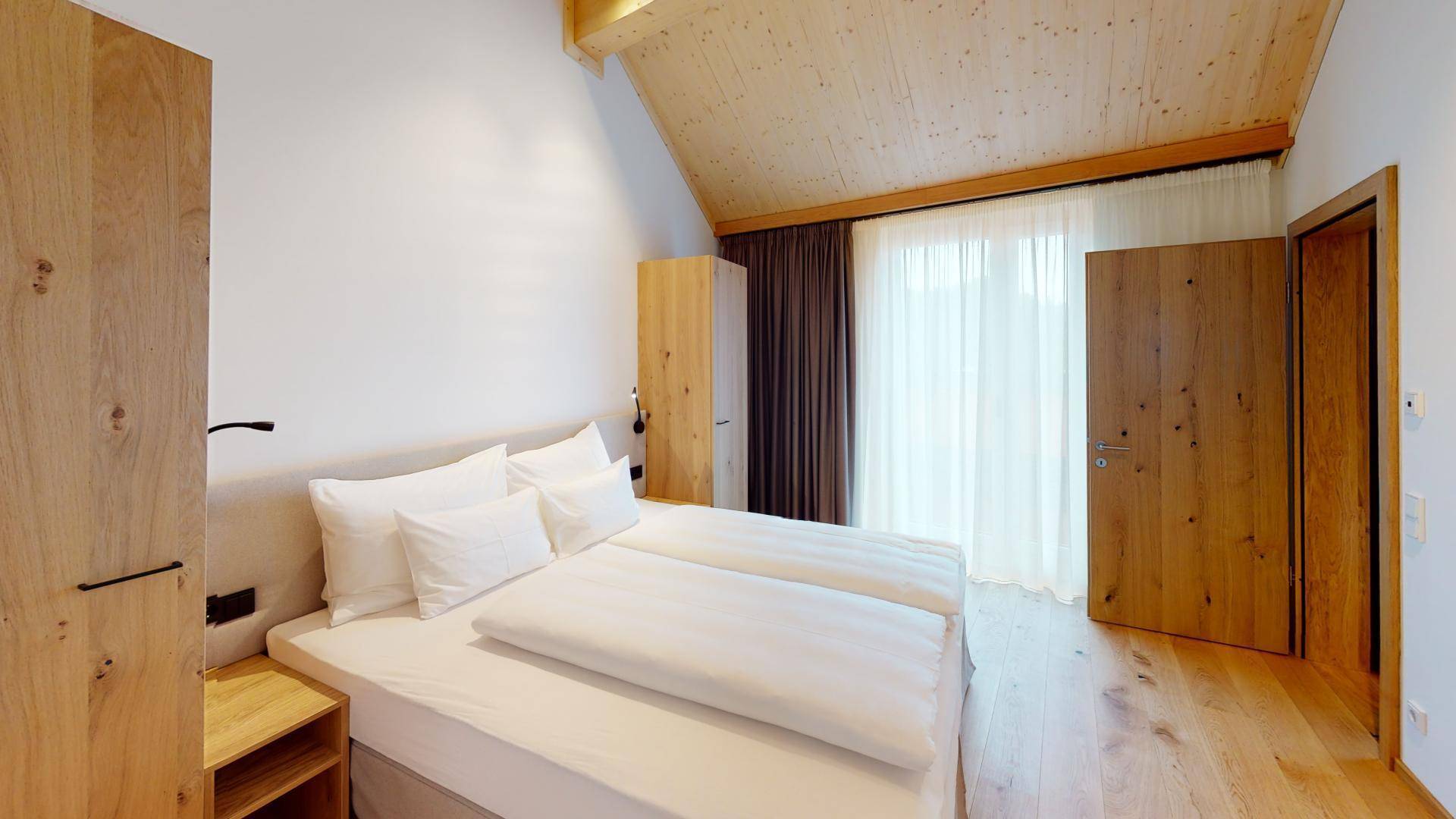 Schlafzimmer mit schräger Holzdecke, Holzboden und Zugang zu einem Außenbereich.