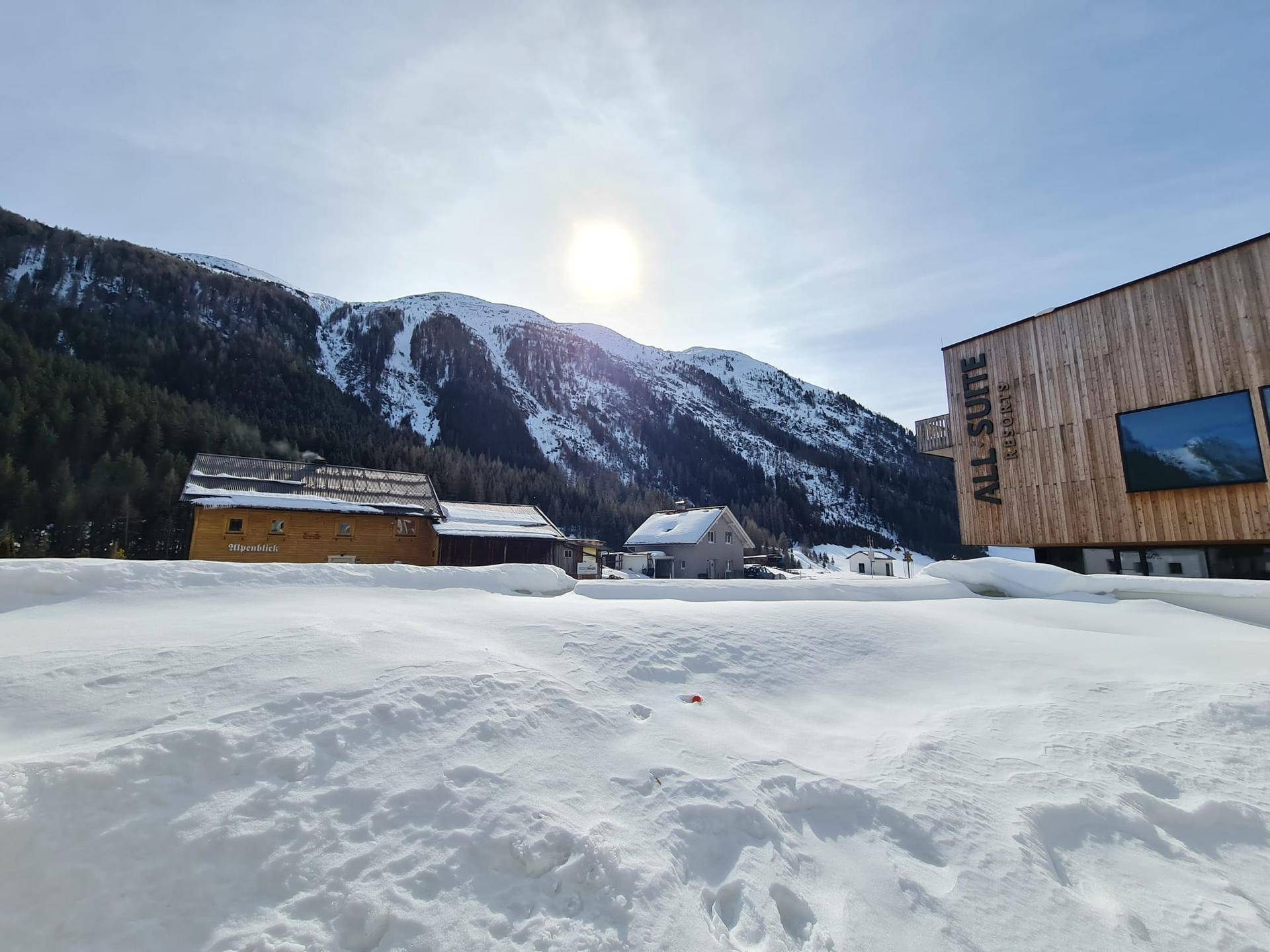 Winterlandschaft mit verschneiten Bergen und modernen Gebäuden unter strahlend blauem Himmel.
