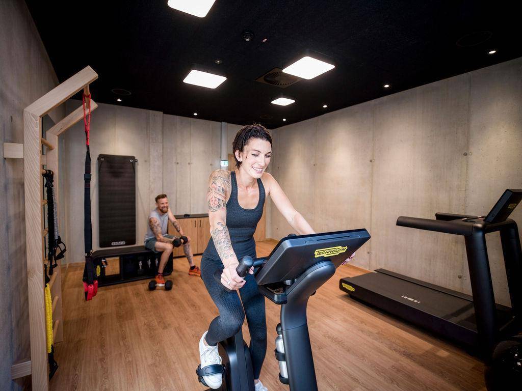 Moderner Fitnessraum mit verschiedenen Trainingsgeräten und Holzboden für sportliche Aktivitäten.