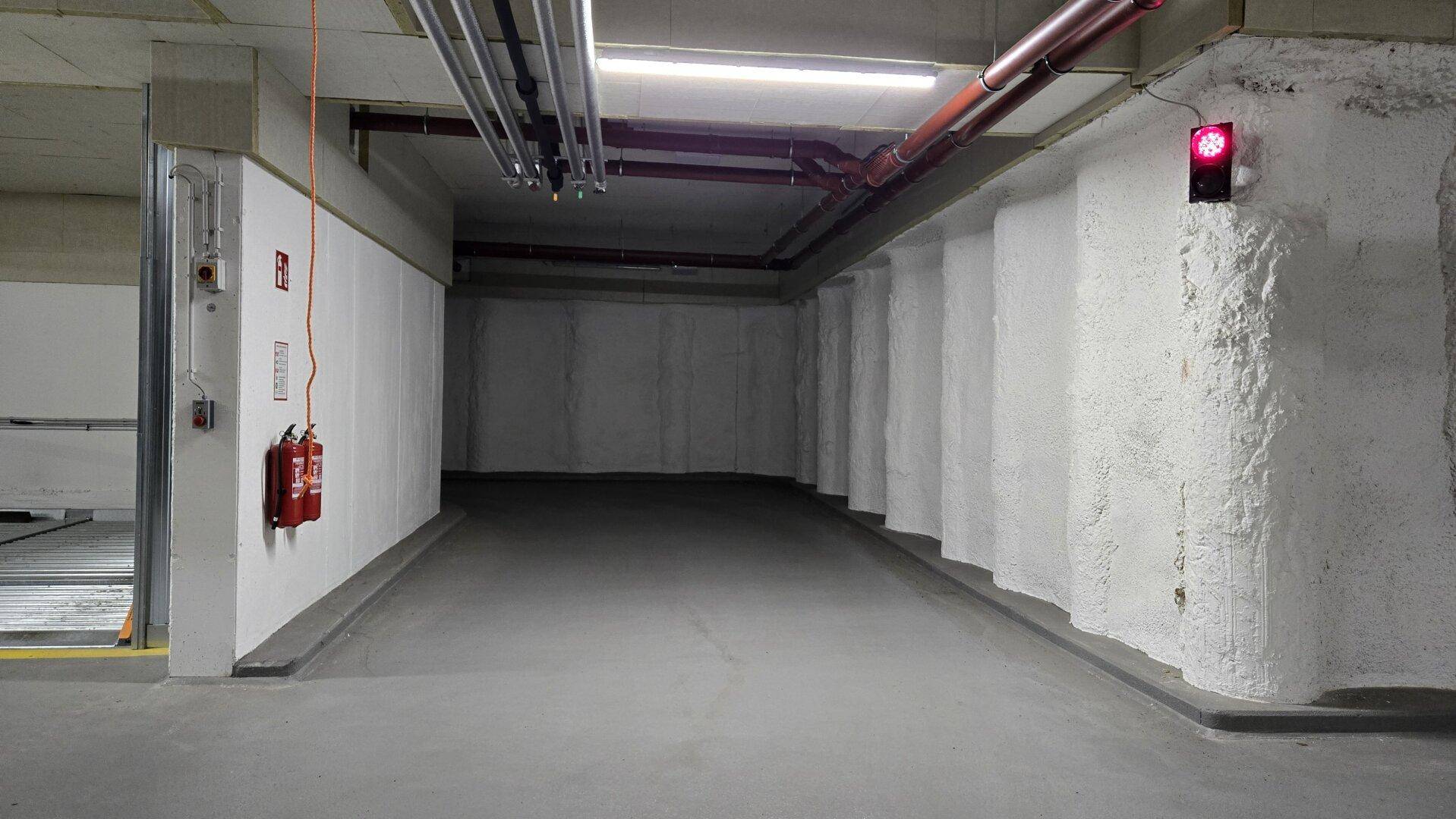 Tiefgarage mit strukturierten weißen Wänden, Betonboden, roten Rohren und einer roten Ampel zur Sicherheit.