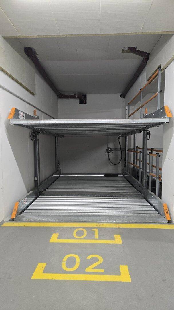 Mechanisches Doppelparkersystem in einer Tiefgarage mit nummerierten Stellplätzen 01 und 02 auf dem Boden.