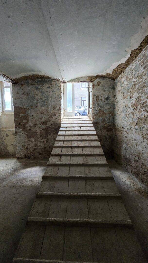 Detailansicht der Holzrampe, die aus dem Kellerraum zur Straße führt, umgeben von rohen Wänden.