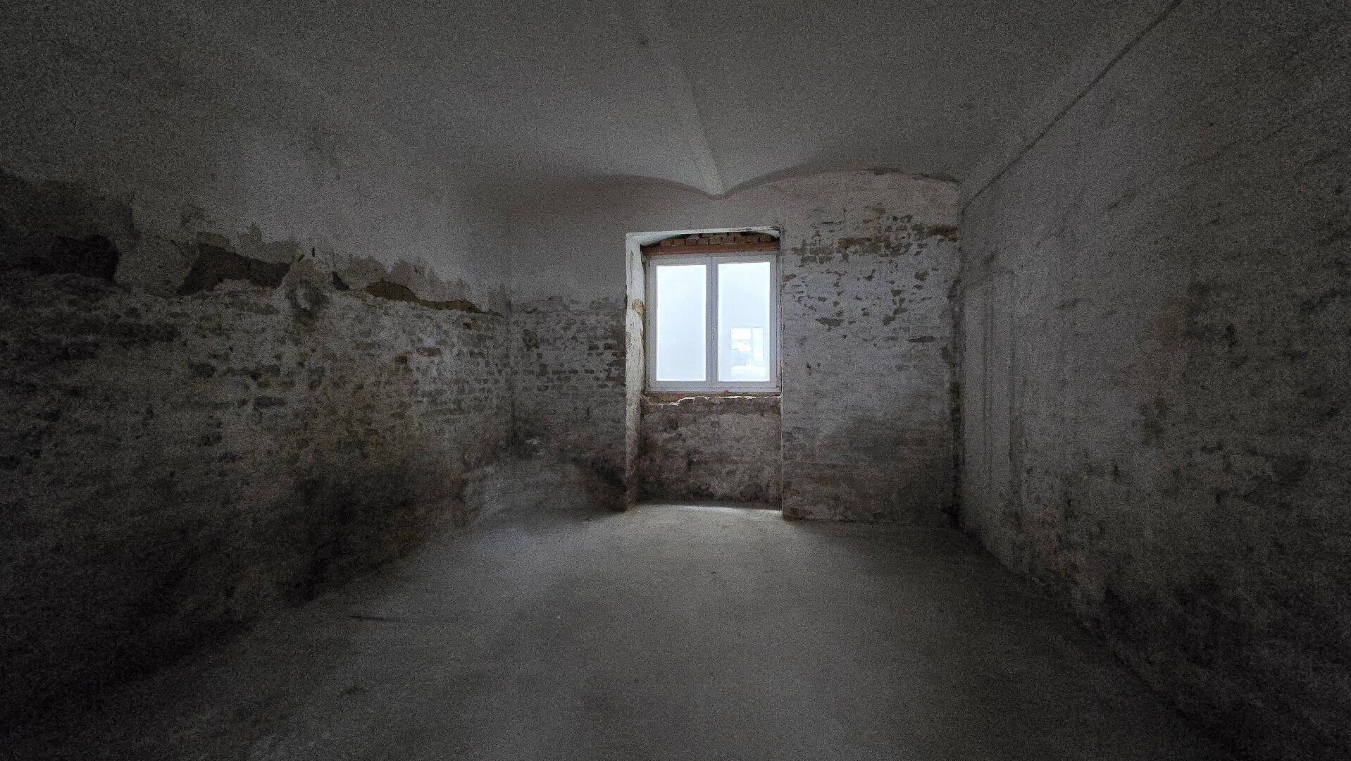 Kleinerer Kellerraum mit einem Fenster, rohen Ziegelwänden und einem einfachen Betonboden.