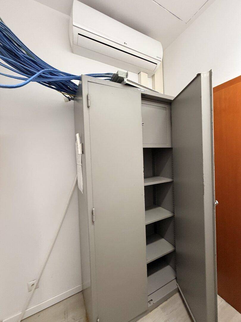 Technikraum mit Klimaanlage und einem Metallschrank, der viele Kabel und Anschlüsse enthält.