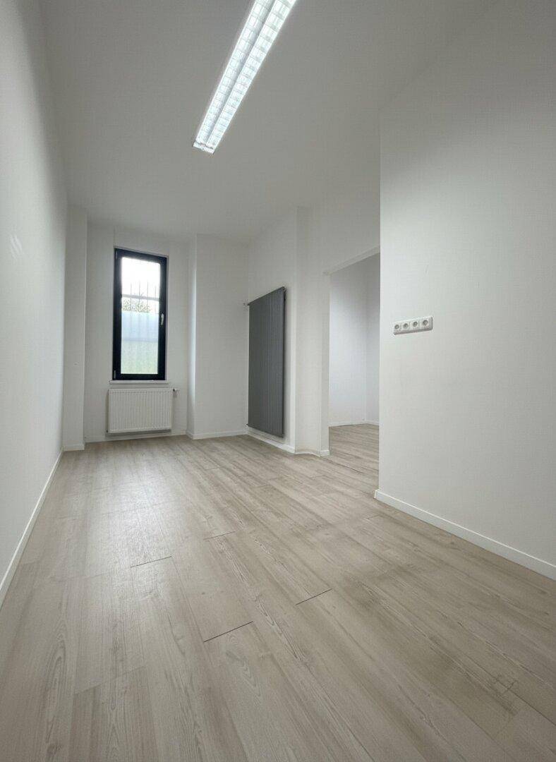 Heller Büroraum mit Laminatboden, einem schmalen Fenster und einem modernen Heizkörper an der Wand.