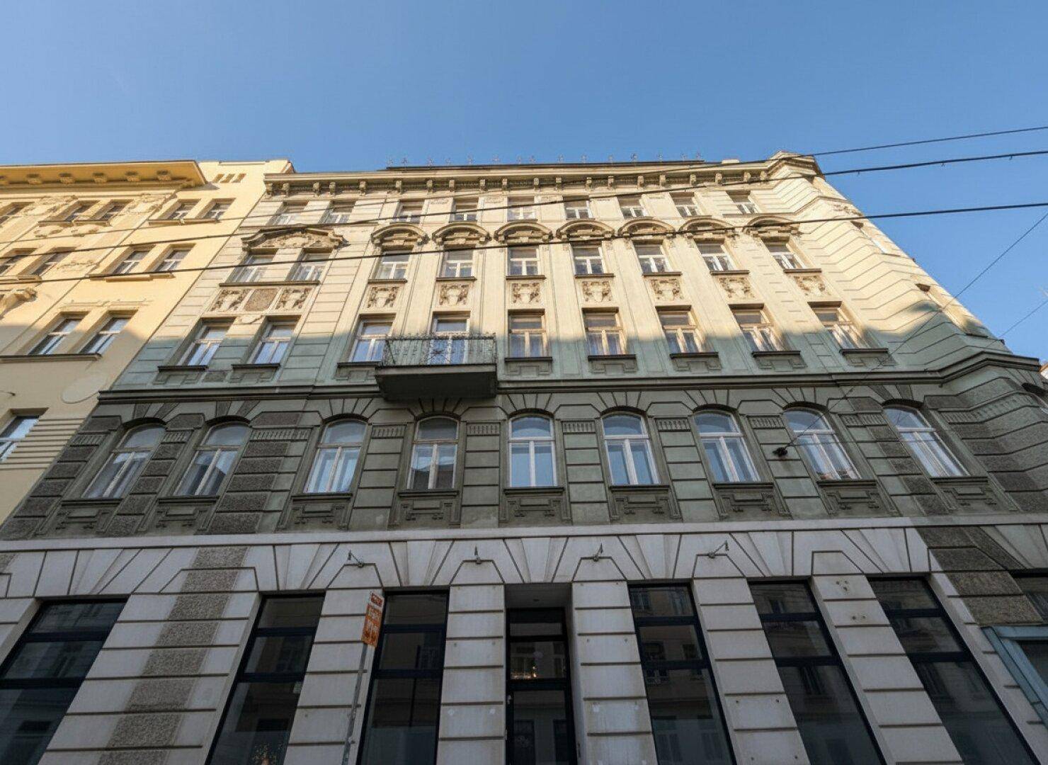 Historisches Gebäude mit klassischer Fassade, vielen Fenstern und einem kleinen Balkon im oberen Bereich.