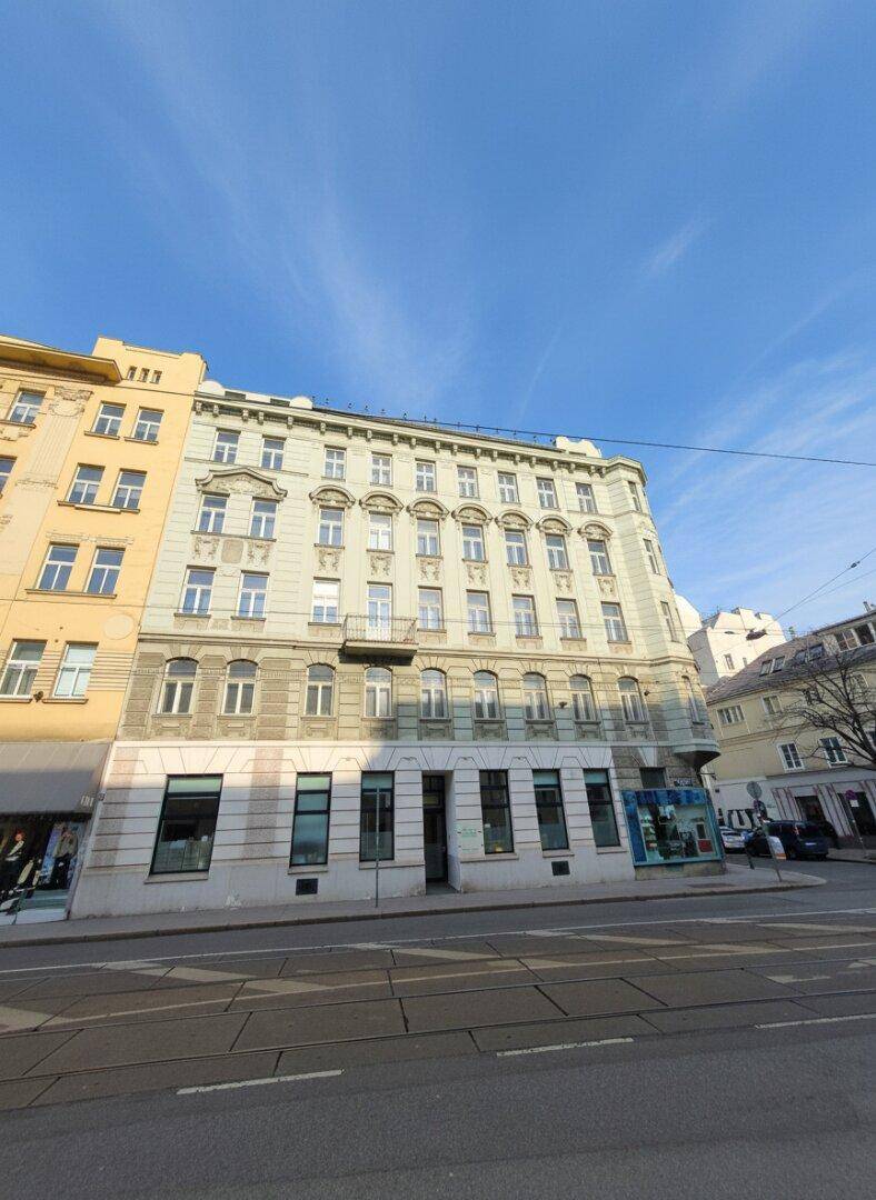 Historisches Gebäude an einer Stadtstraße mit Geschäften im Erdgeschoss und vielen Fenstern.
