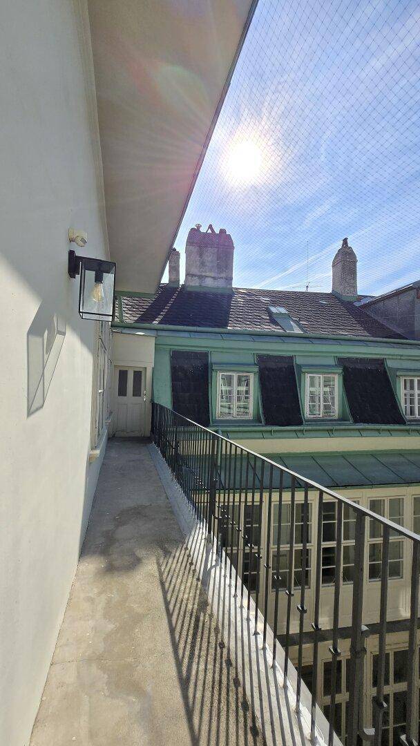 Sonniger Balkon mit schmiedeeisernem Geländer und Blick auf die umliegenden Dächer.