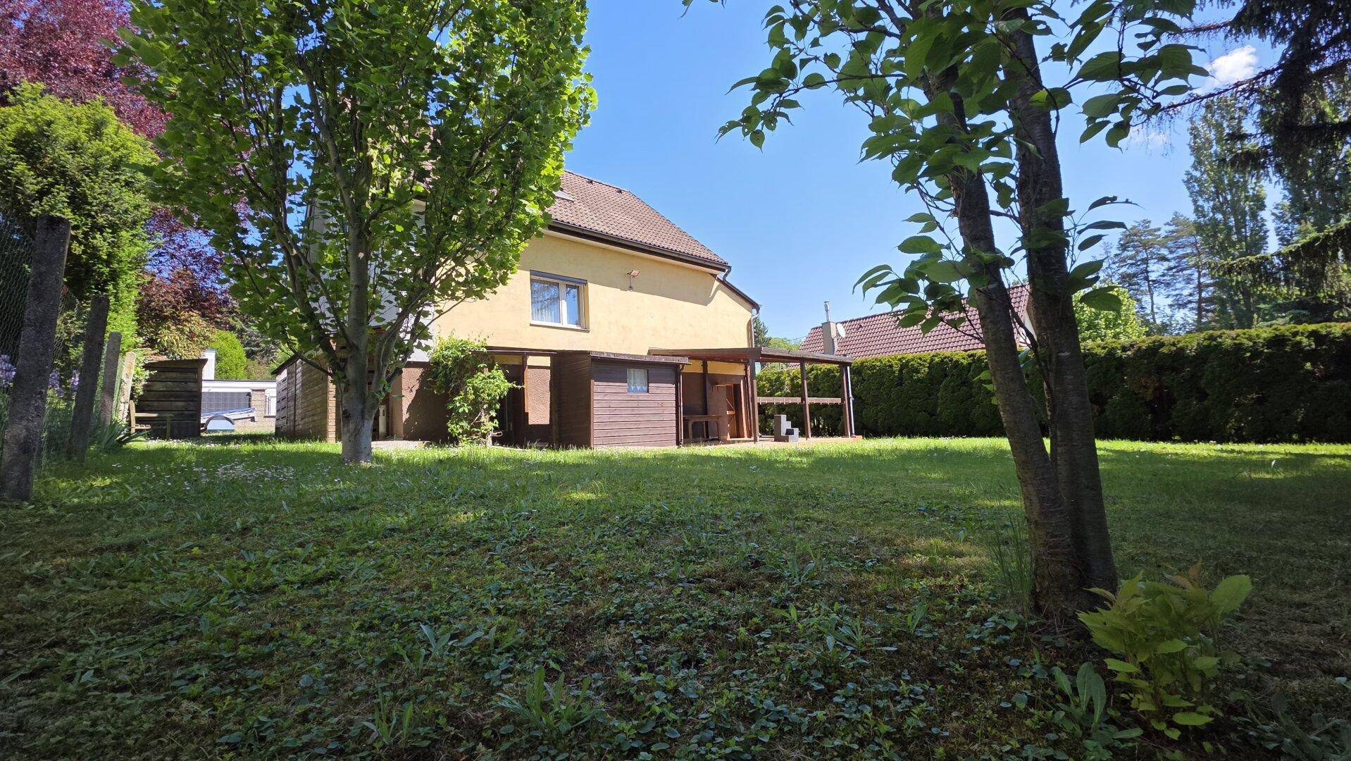 Rückansicht eines gelben Hauses mit überdachter Terrasse und weitläufigem Gartenbereich.