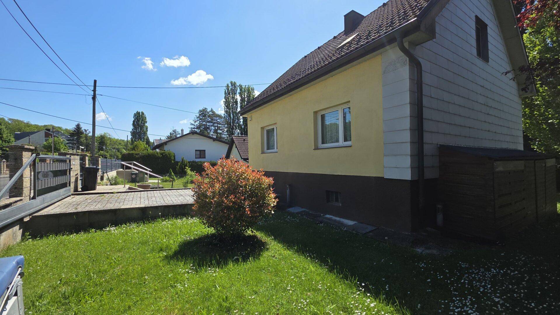 Seitenansicht des gelben Hauses mit gepflastertem Bereich und einem kleinen Zierstrauch.