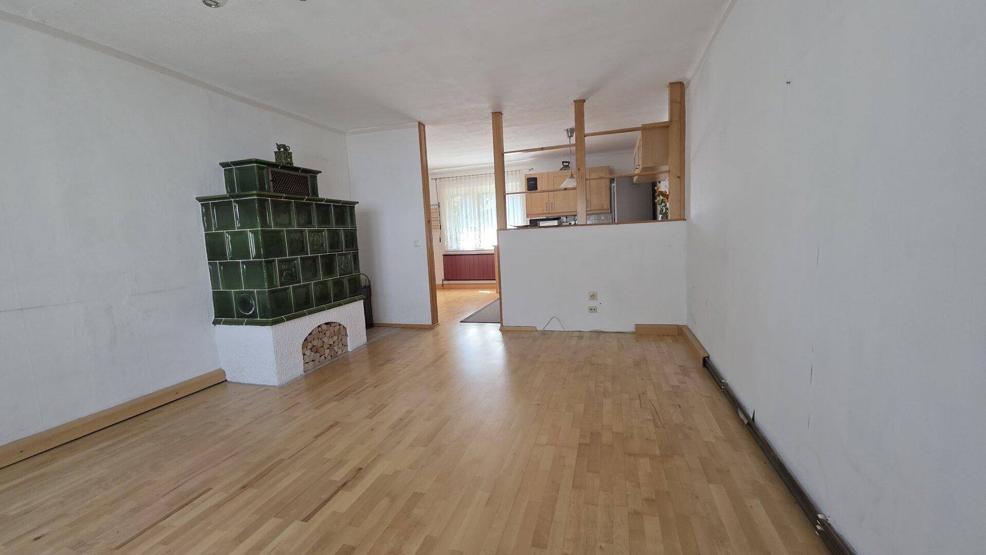 Helles Wohnzimmer mit traditionellem Kachelofen und hellem Parkettboden, offen zur Küche.