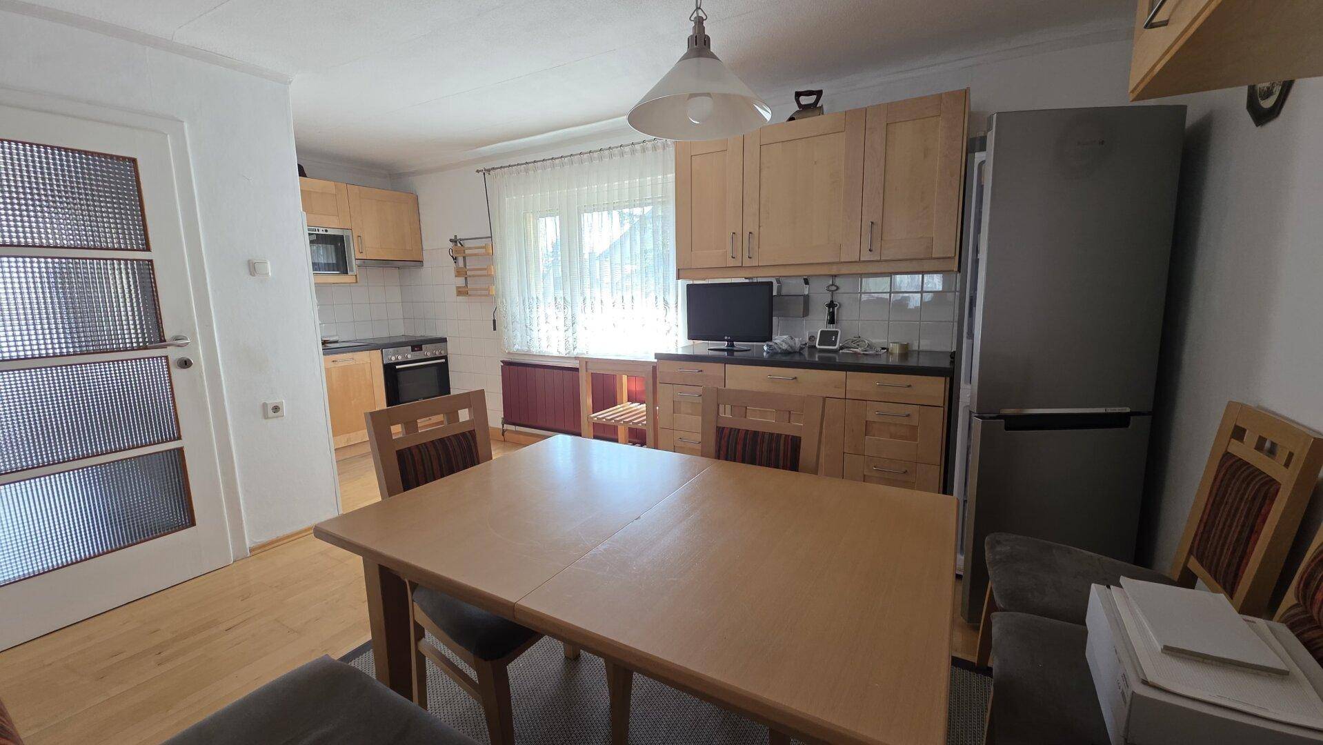 Gemütliche Wohnküche mit Esstisch, Holzmöbeln und einem modernen Kühlschrank.