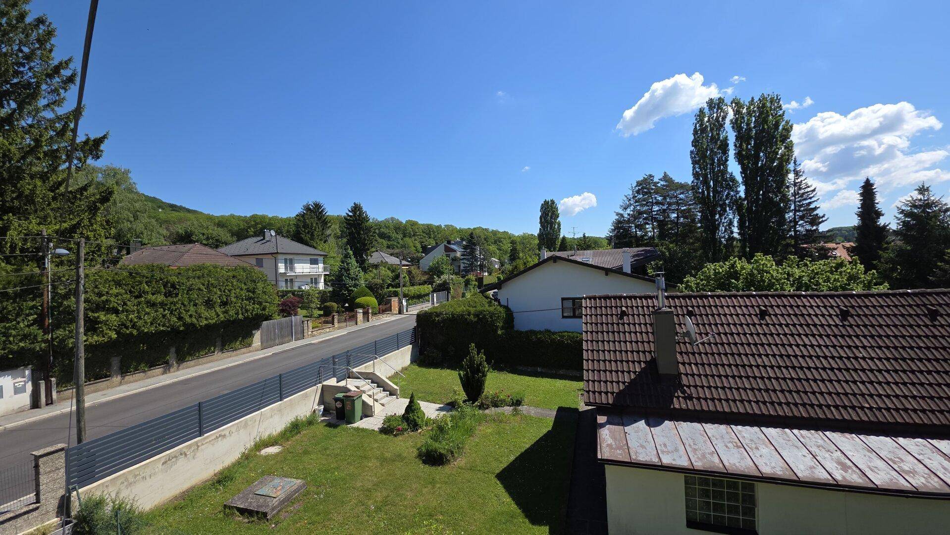 Weitläufiger Blick über eine Wohnsiedlung mit Straße und grünen Hügeln im Hintergrund.