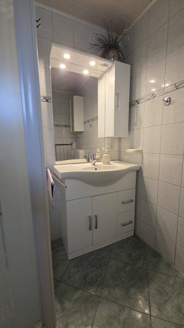 Badezimmer mit Waschtisch, Spiegelschrank und hellen Fliesen an Wänden und Boden.