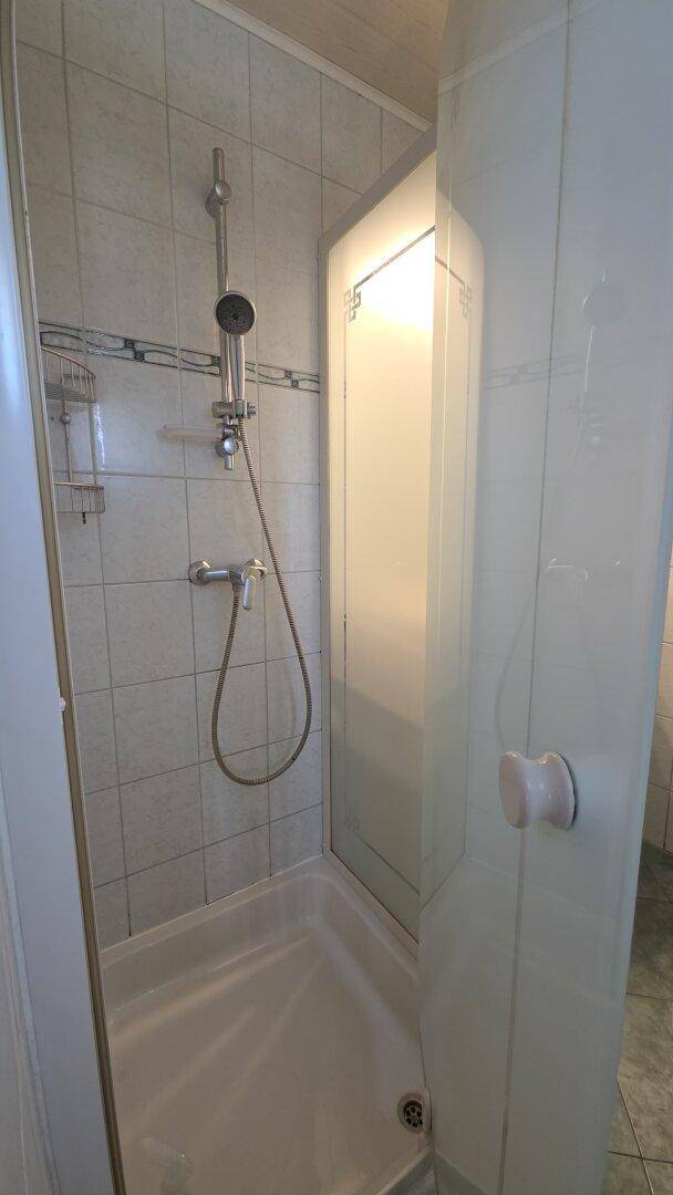 Duschbereich im Badezimmer mit hellen Fliesen und einfacher Duschkabine.