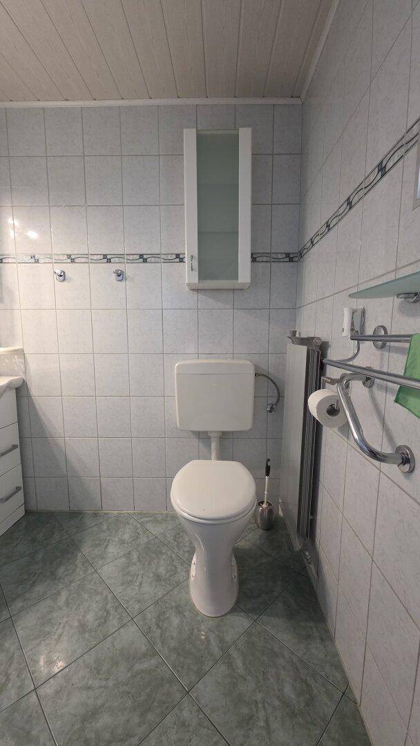 Toilettenbereich im Badezimmer mit Wand-WC, Heizkörper und hellen Fliesen.