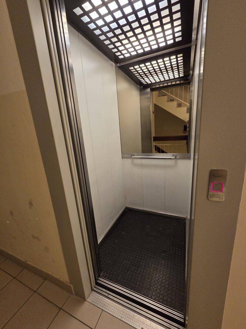 Moderner Aufzug im Gebäude mit Spiegelfläche und Blick auf das Treppenhaus.