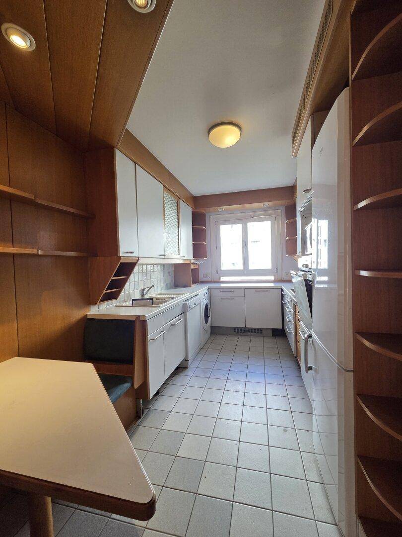 Helle Küche mit weißen Schränken, Holzelementen und Essbereich, mit Fenster und Fliesenboden.