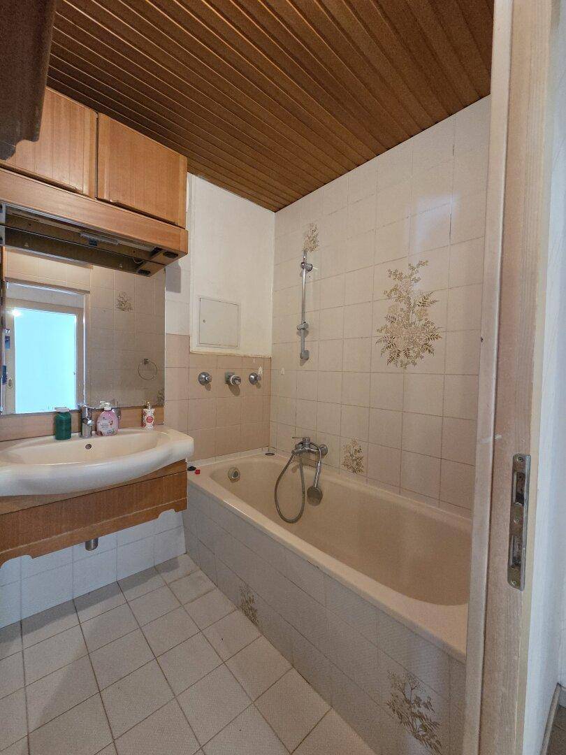 Badezimmer im 80er-Jahre-Stil mit Badewanne, Waschbecken und Holzdecke.