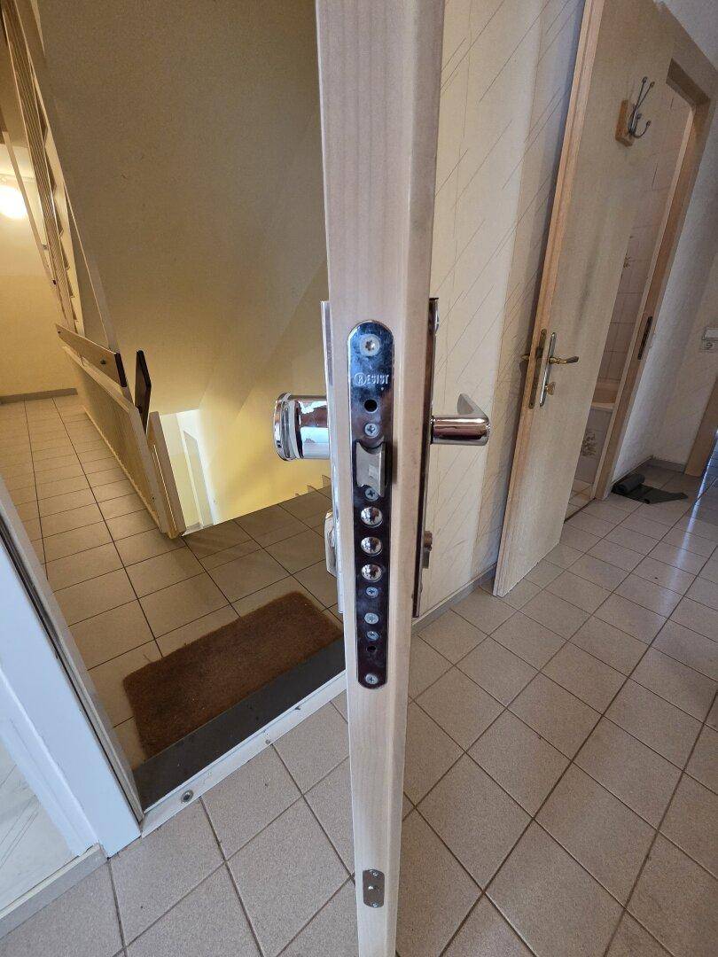 Eingangsbereich mit Sicherheitstür und Blick auf eine Treppe, gefliestem Boden.