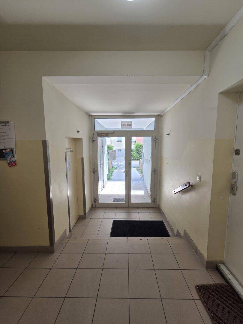 Heller Eingangsbereich mit Fliesenboden und Glastür, die ins Freie führt.